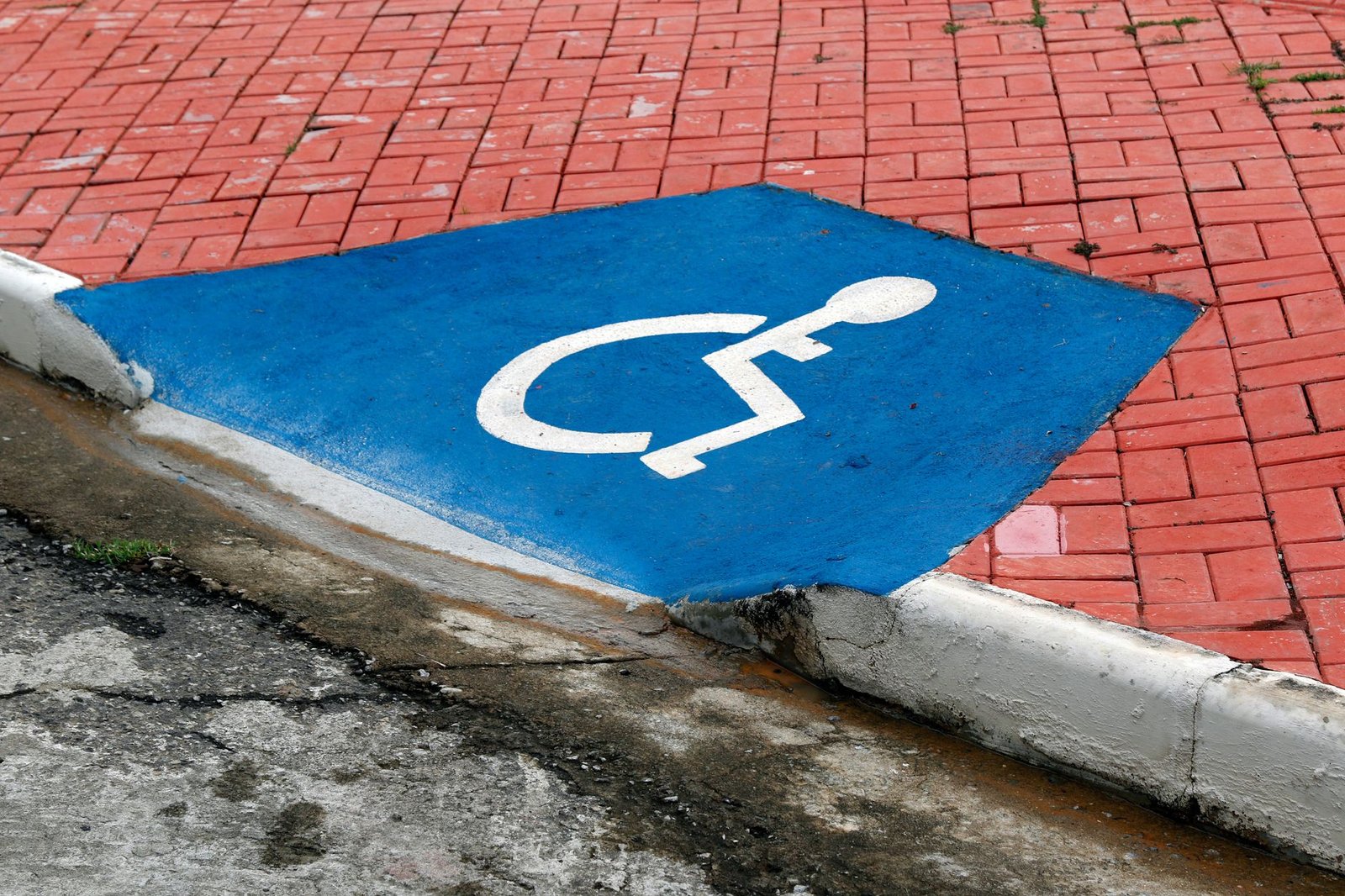 Rebaixamento de calcada com o simbolo internacional de acesso pintado em azul, junto ao meio-fio