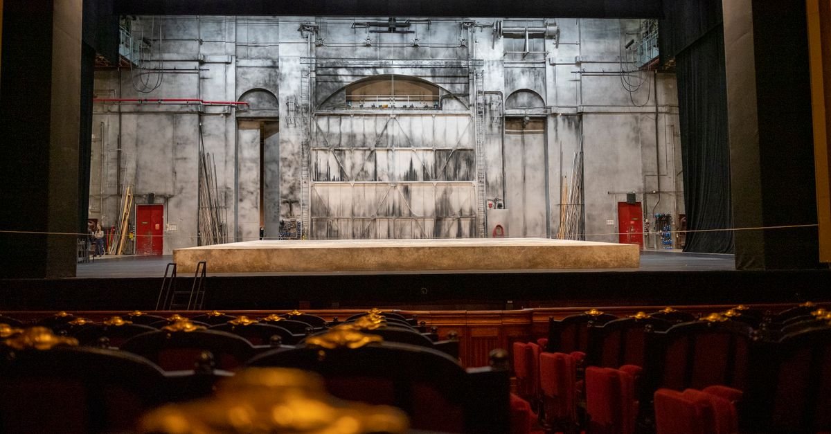 Palco vazio de teatro visto da plateia com poltronas em primeiro plano