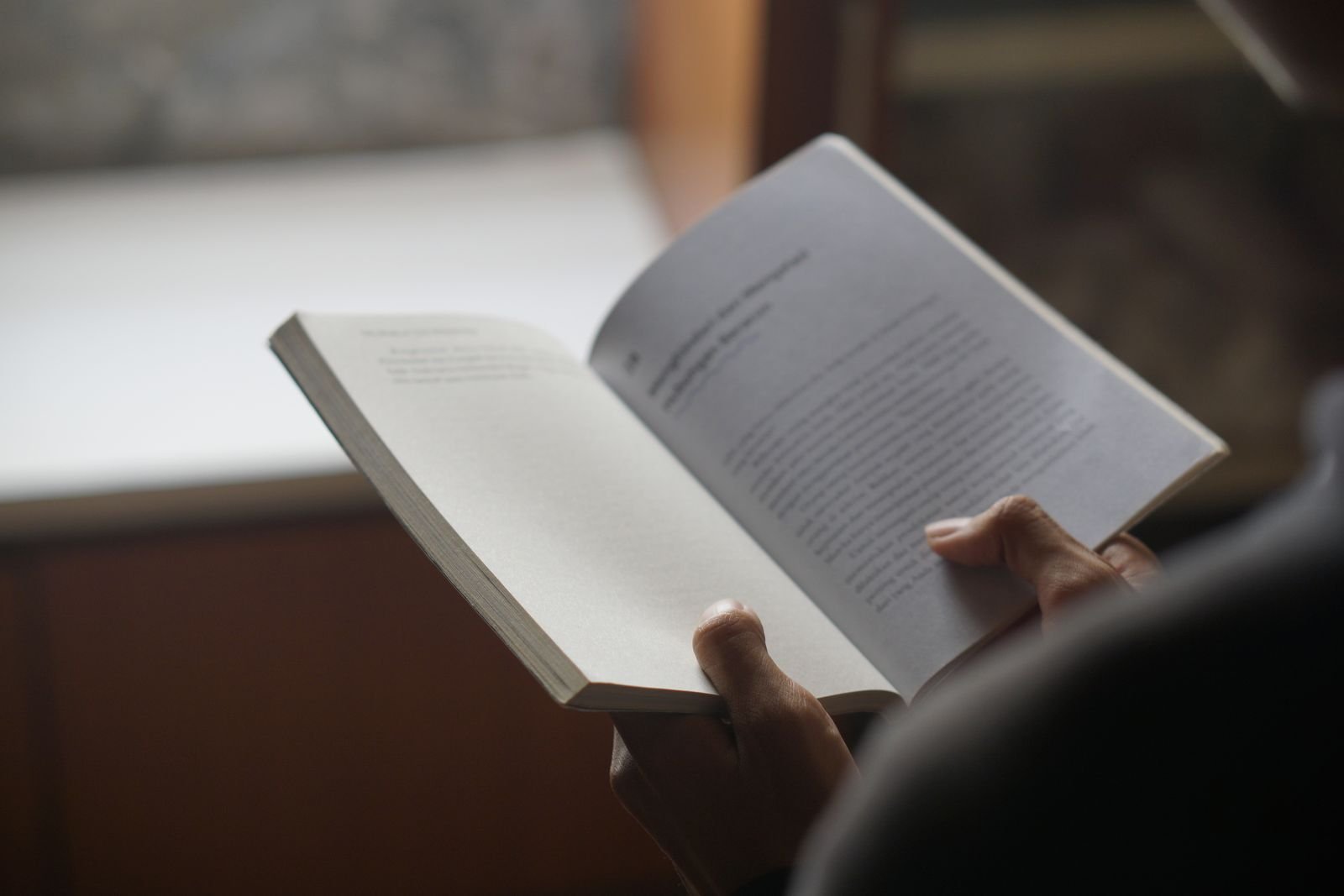 Pessoa segura um livro aberto com as duas mãos durante a leitura