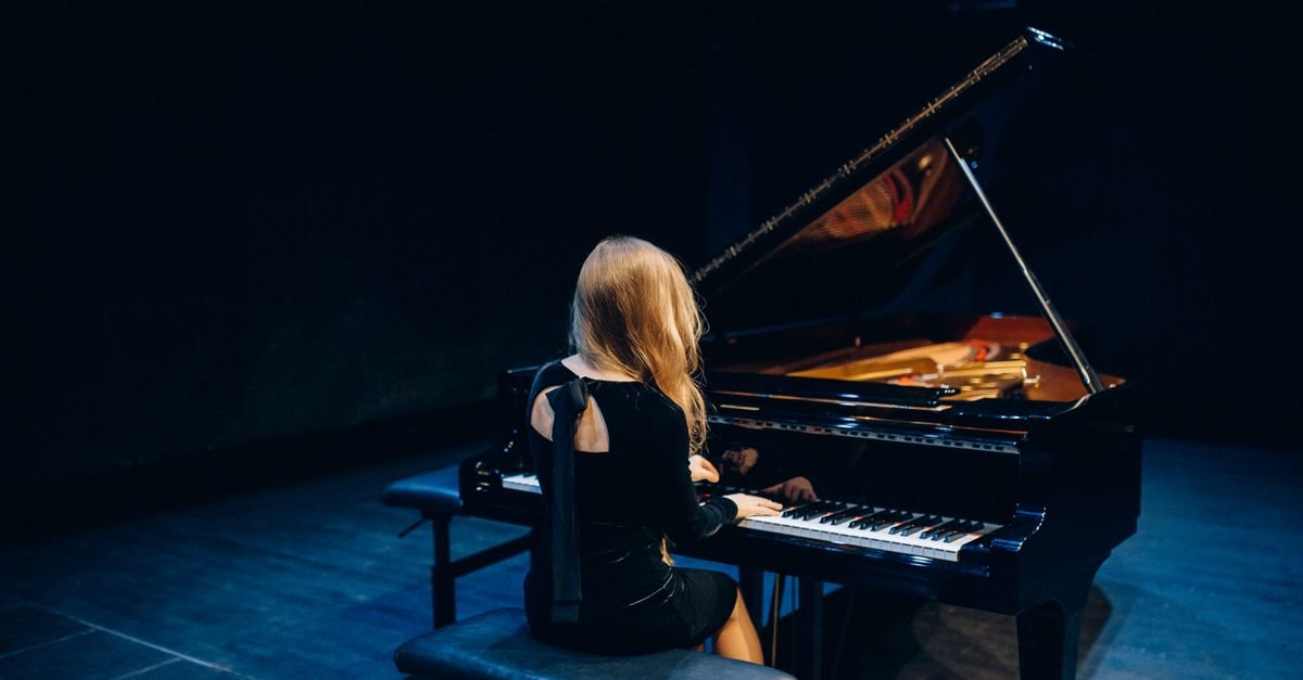 Pianista sentada ao piano de cauda em palco escuro durante apresentação musical