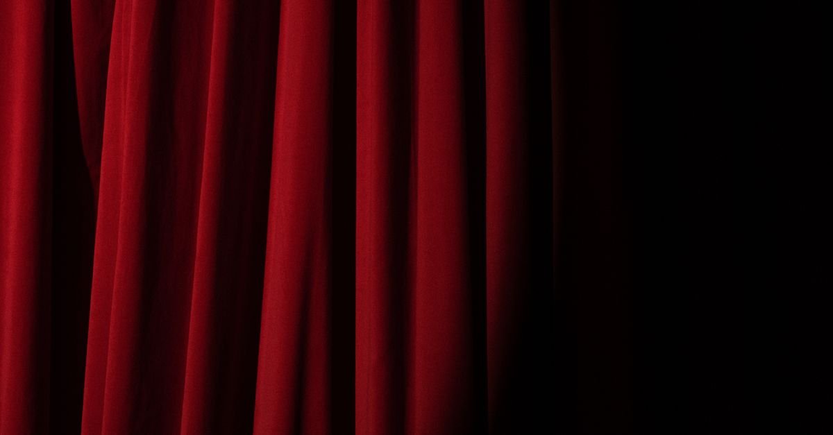 Cortina de veludo vermelho de teatro iluminada de lado, em plano fechado