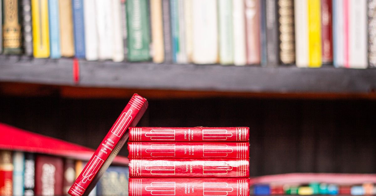 Livros de capa vermelha empilhados diante de uma estante de livraria