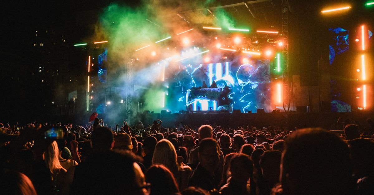 Público em frente a palco de festival de música eletrônica à noite, com luzes coloridas e telão