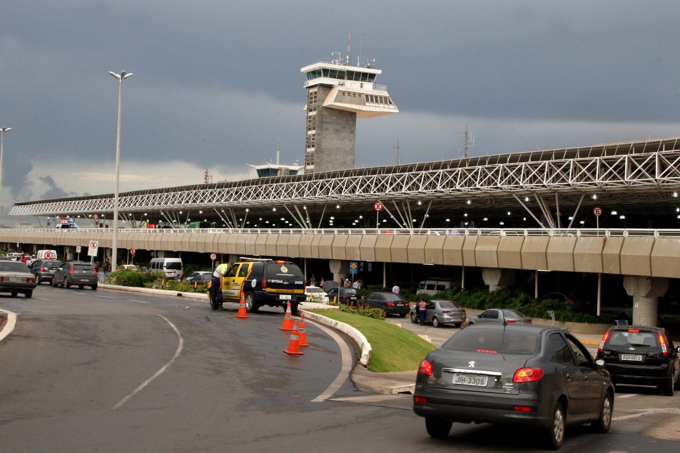 Via de acesso ao Aeroporto Internacional de Brasília com carros, viatura do BPTran e a torre de controle ao fundo