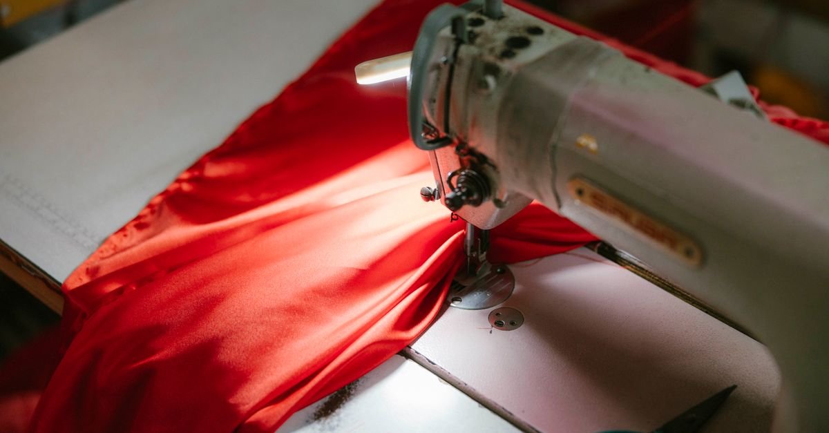 Maquina de costura industrial costurando um tecido vermelho sob luz direta em bancada de oficina