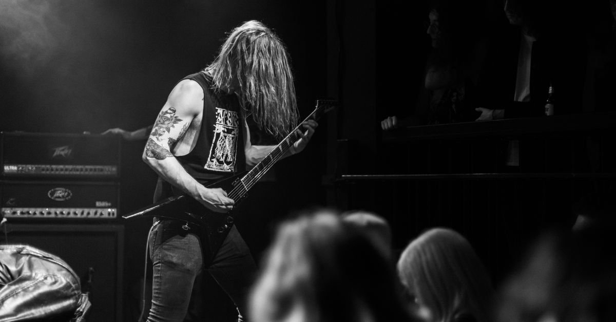 Guitarrista de costas tocando em palco de casa de shows, em foto preto e branco
