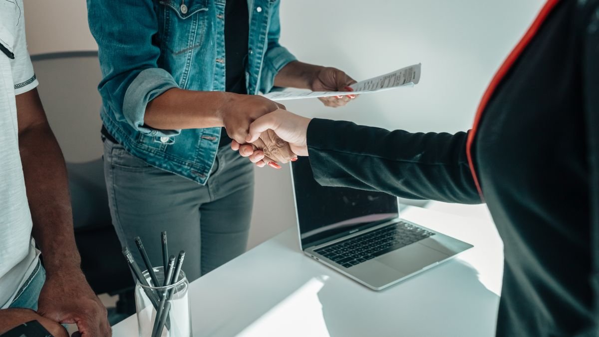Aperto de mãos sobre mesa de escritório durante entrevista de emprego, com currículo e notebook