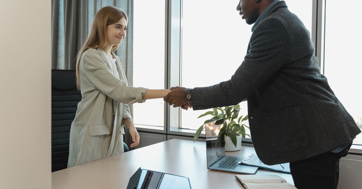 Duas pessoas apertam as maos sobre uma mesa de escritorio ao fim de uma entrevista de emprego