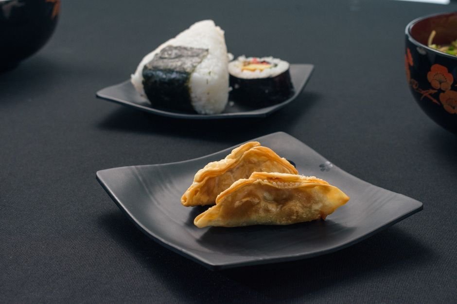 Guioza, bolinho de arroz e sushi servidos em pratos escuros
