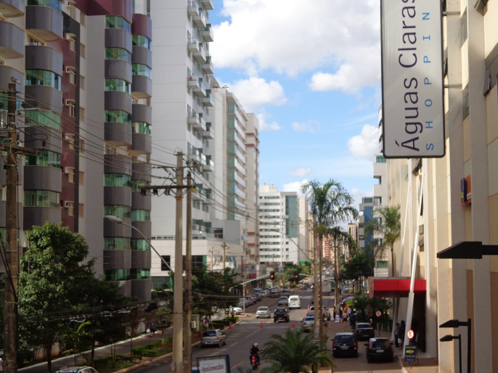 Avenida das Castanheiras, em Águas Claras, com prédios altos dos dois lados, carros na pista e placa do shopping da cidade