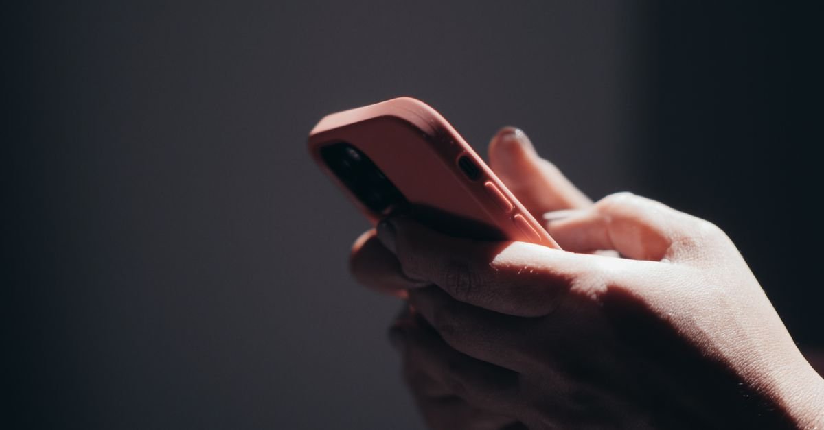 Mãos segurando um celular em ambiente de pouca luz, com a tela voltada para o usuário