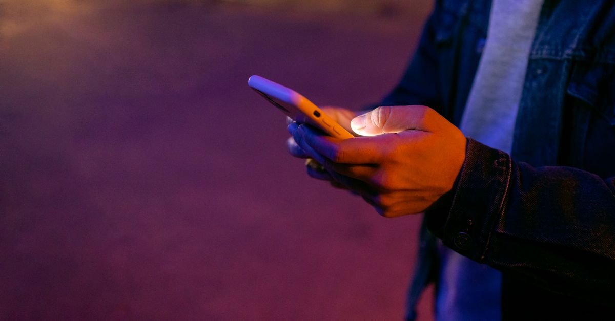 Mãos segurando um celular iluminado durante a noite em ambiente urbano