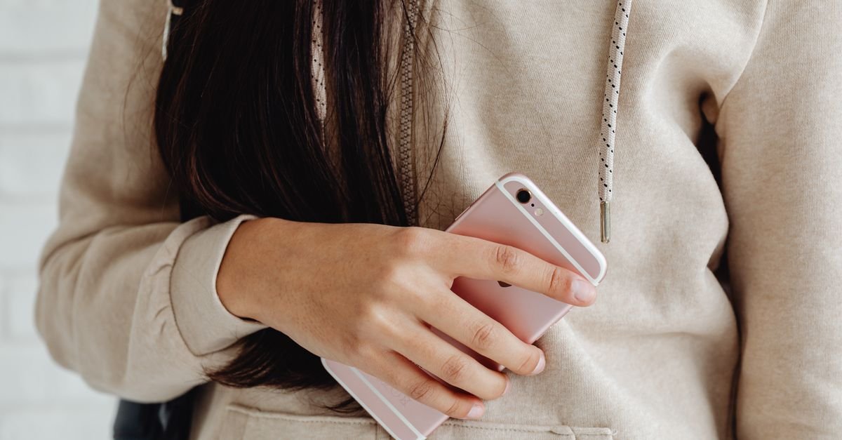 Mão segurando um celular rosa junto ao corpo, com a tela voltada para baixo