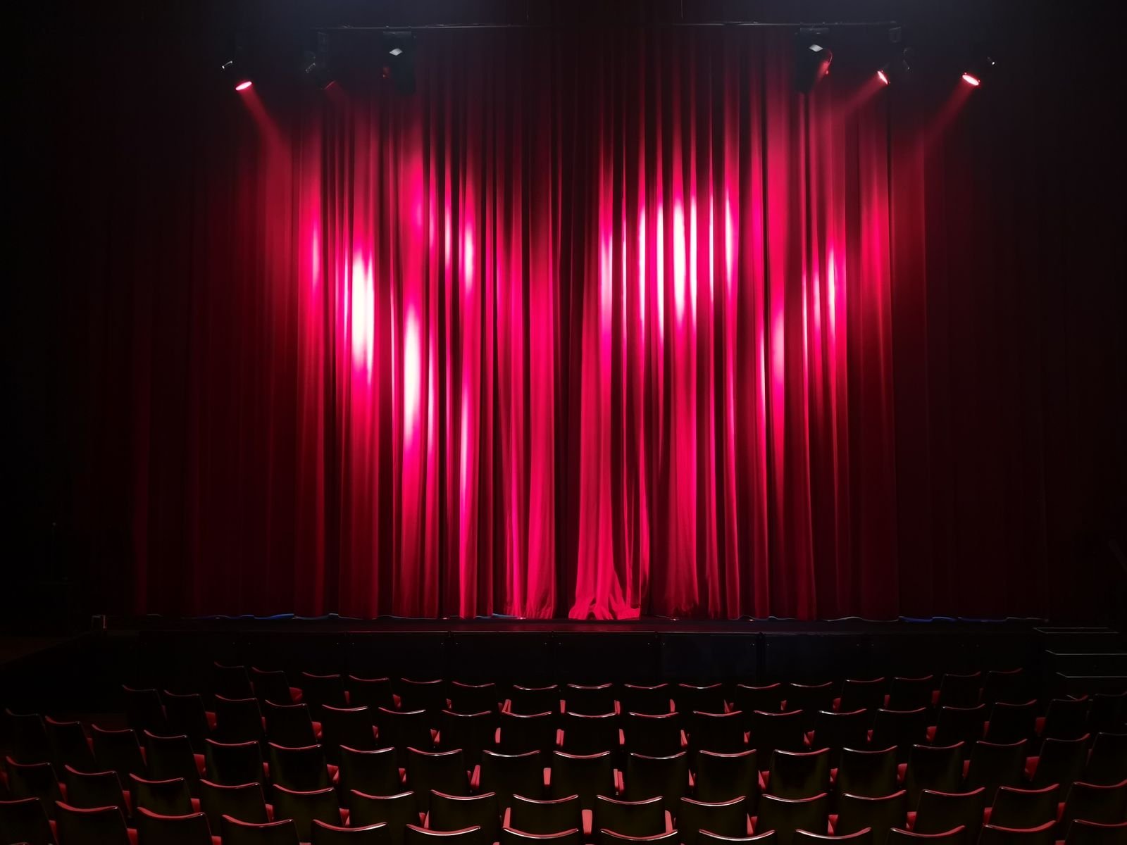Palco de teatro vazio com cortina vermelha e fileiras de poltronas à frente