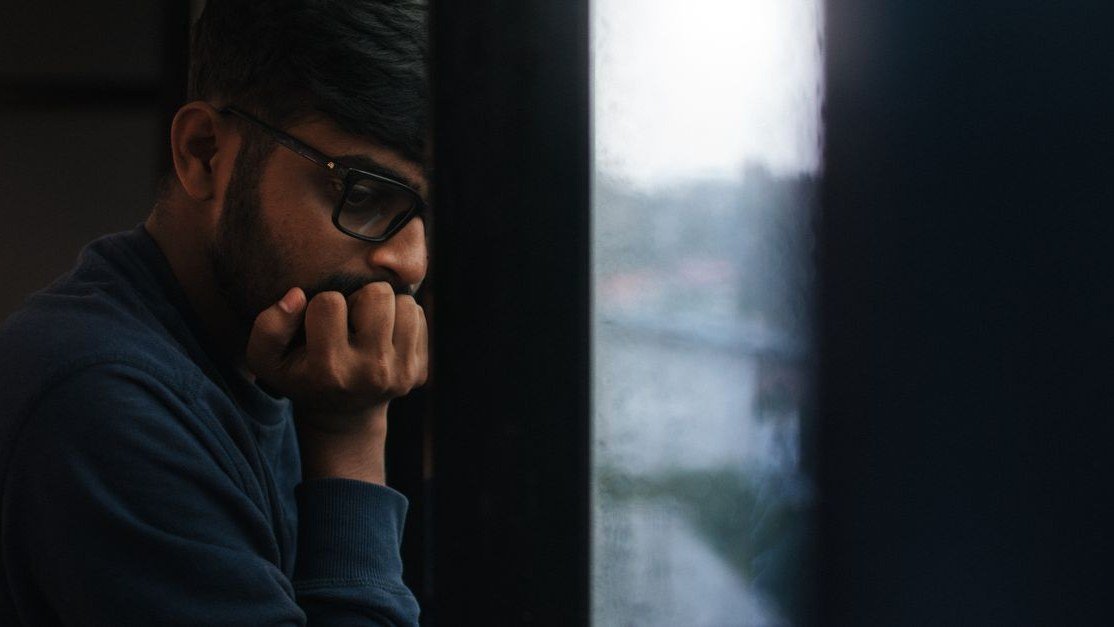 Homem observa a chuva pela janela, apoiado na mão