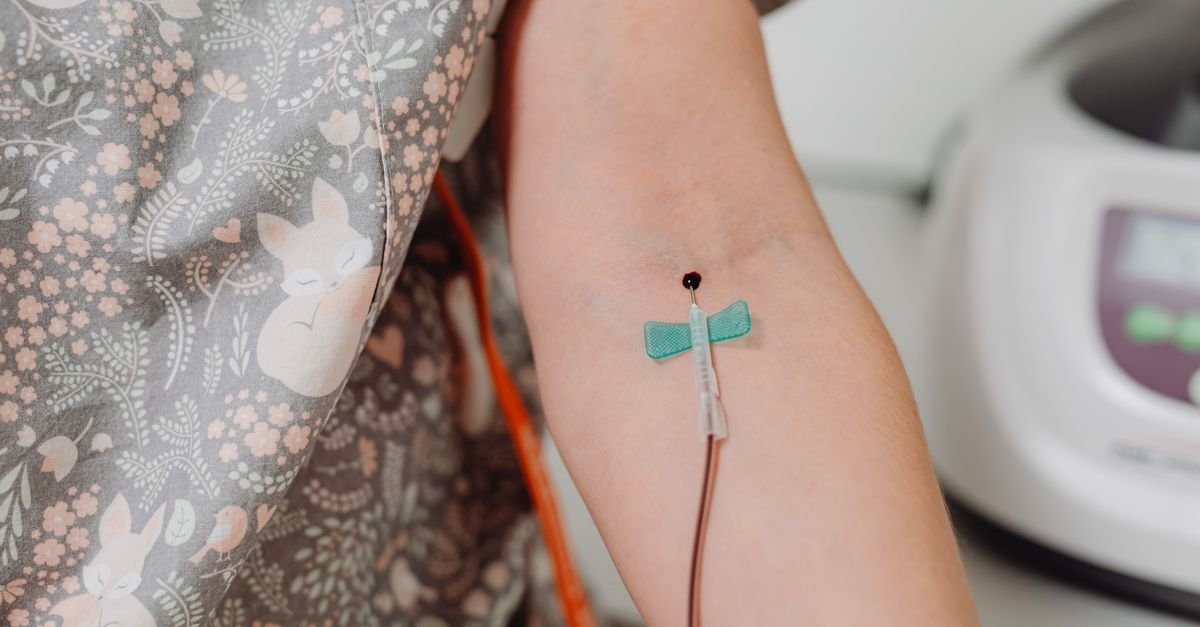 Close de cateter intravenoso fixado no braço de um paciente em atendimento