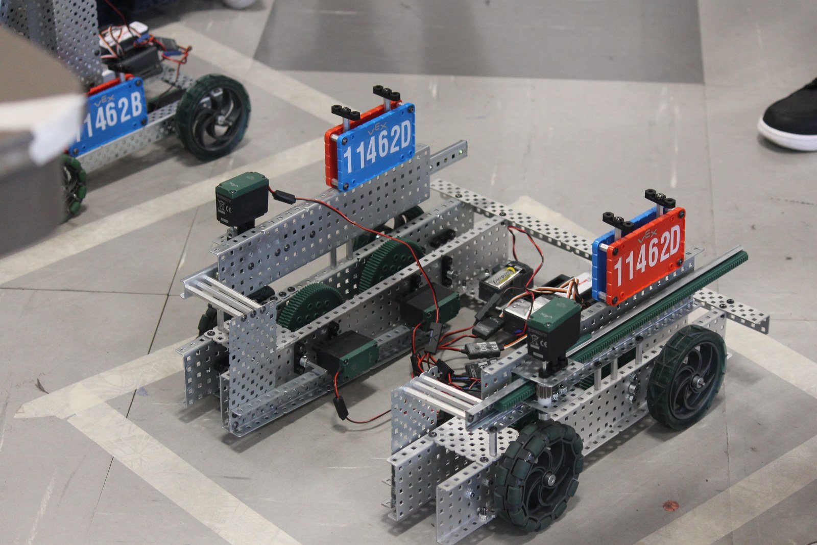 Dois robôs de competição de robótica montados em estrutura de metal, com placas numeradas