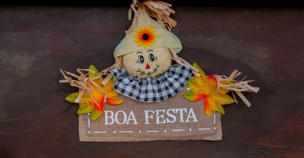 Enfeite junino de espantalho com chapéu de palha e placa escrita Boa Festa