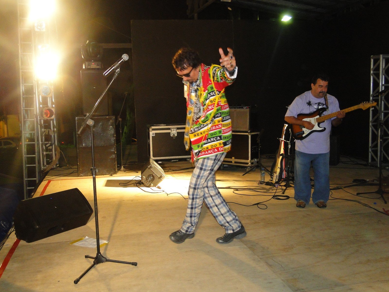 O cantor cearense Falcão em show, de óculos escuros e roupa colorida, ao lado do guitarrista no palco