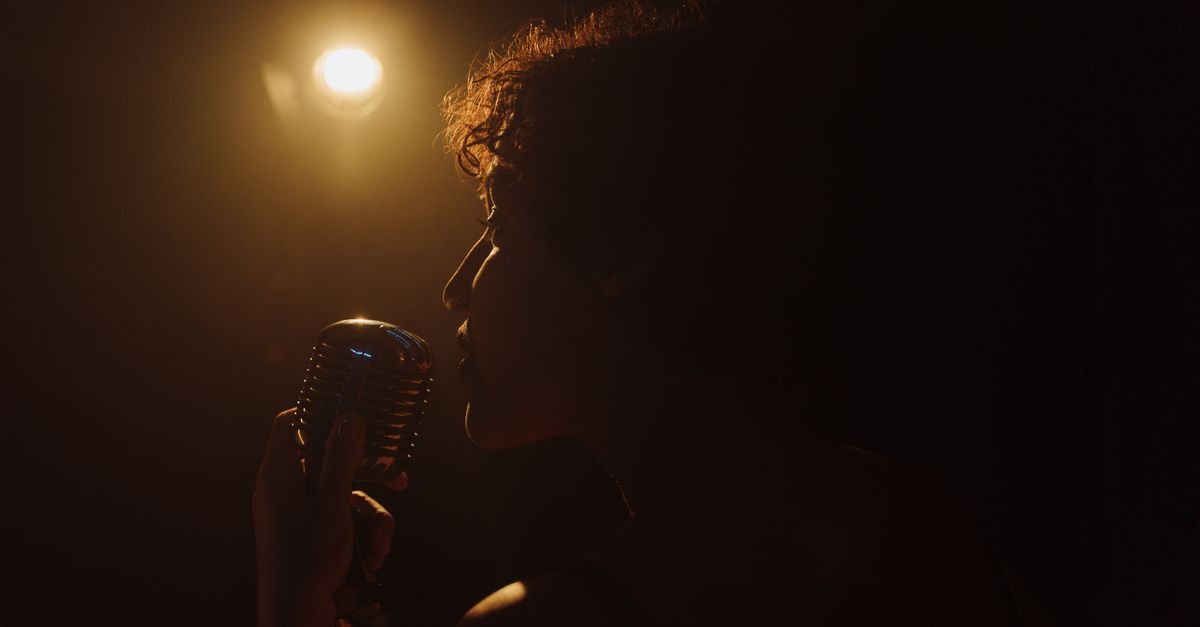 Silhueta de intérprete cantando em microfone antigo sob refletor quente no palco