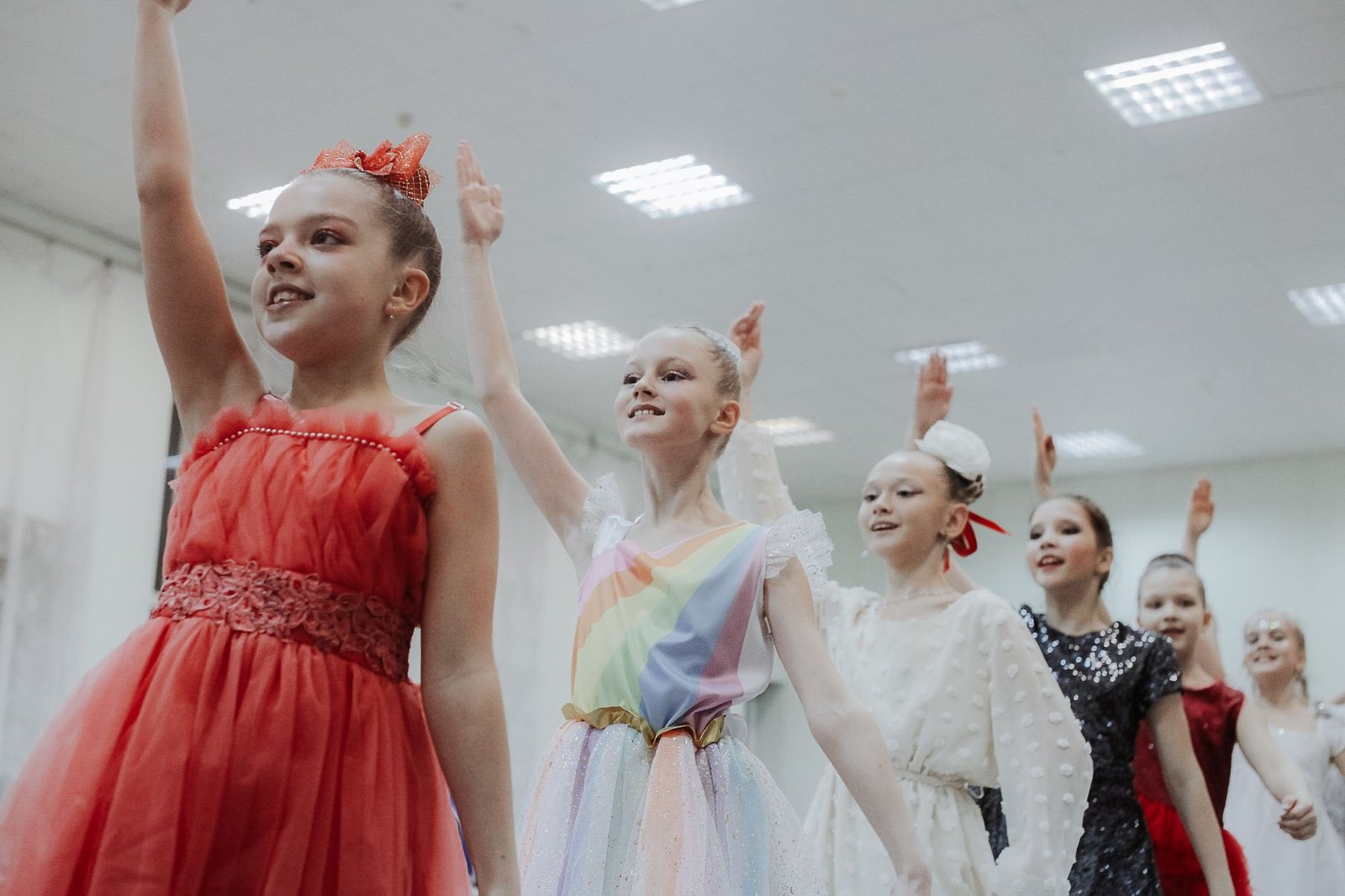 Grupo de meninas de vestidos coloridos com os braços erguidos durante ensaio de ballet, em foto de arquivo