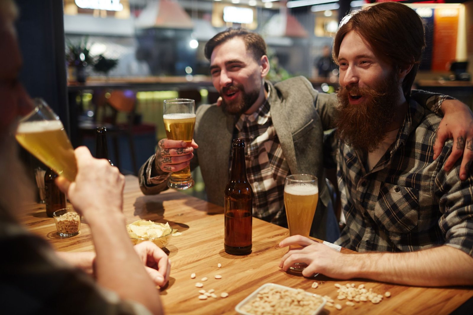 Amigos brindam com chope em uma mesa de bar com amendoim e batata chips