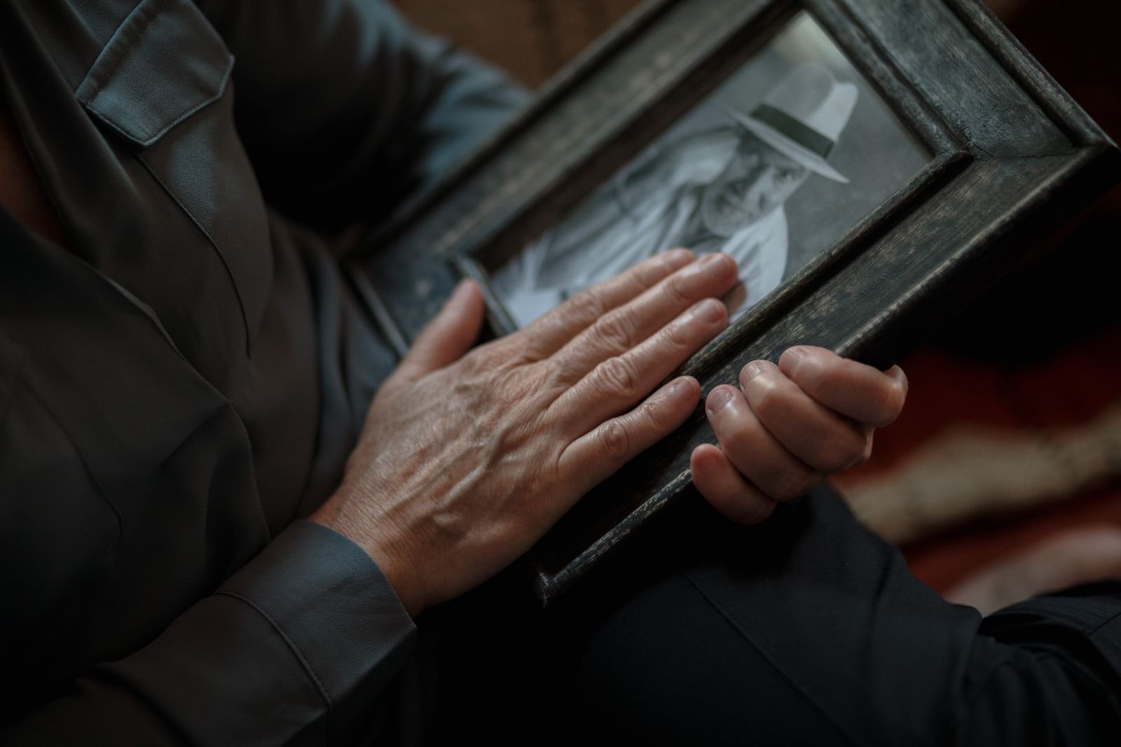 Mãos de uma pessoa idosa sobre um porta-retrato com fotografia antiga em preto e branco