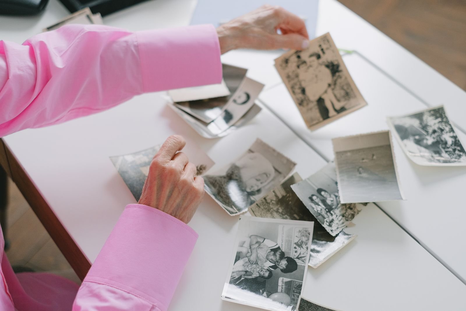 Mãos de uma mulher idosa separando fotografias antigas em preto e branco sobre uma mesa