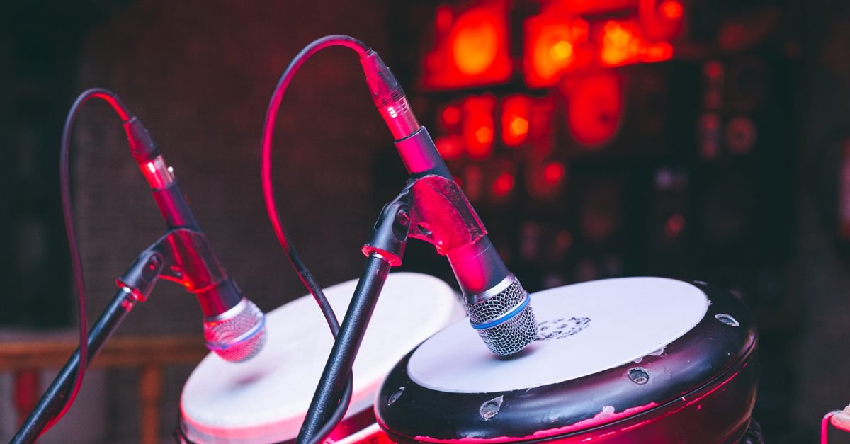 Dois tambores de percussao com microfones posicionados sobre as peles, em palco iluminado de vermelho