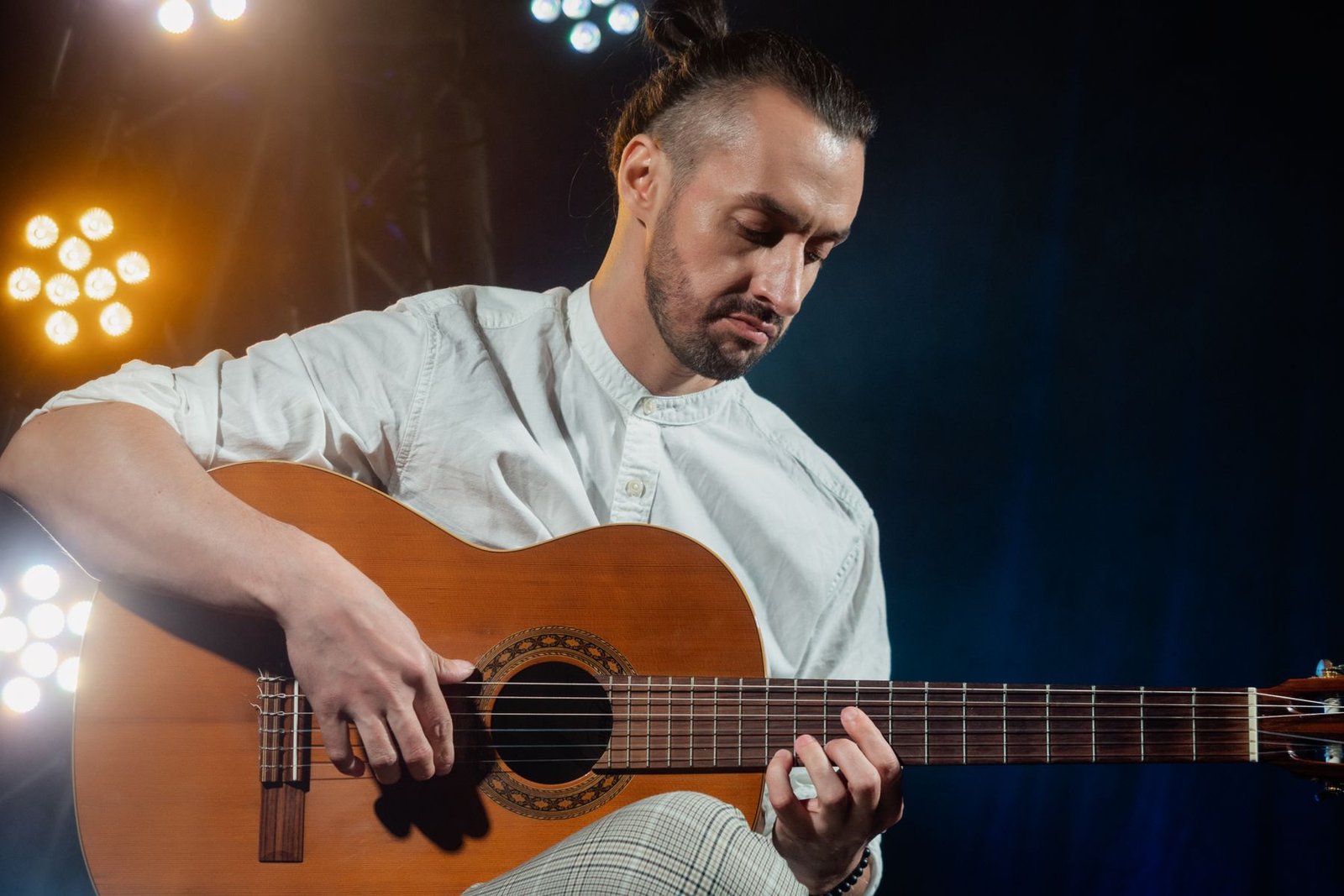 Violonista de camisa branca toca violão de cordas de náilon sob luzes de palco (foto ilustrativa de banco de imagens)
