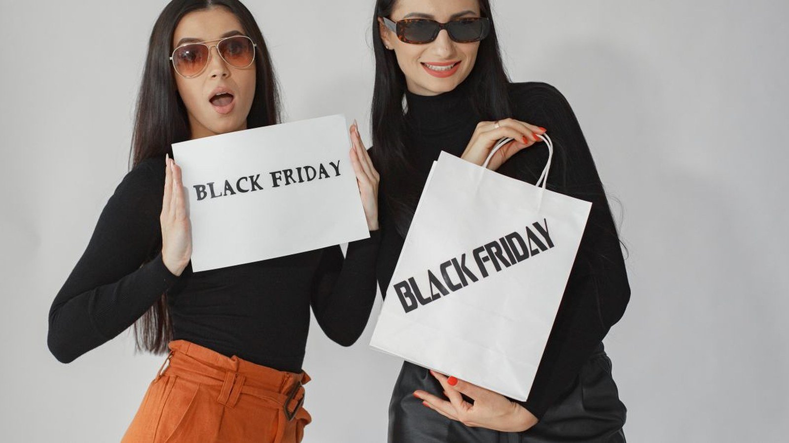 Duas mulheres seguram uma placa e uma sacola de compras com os dizeres Black Friday