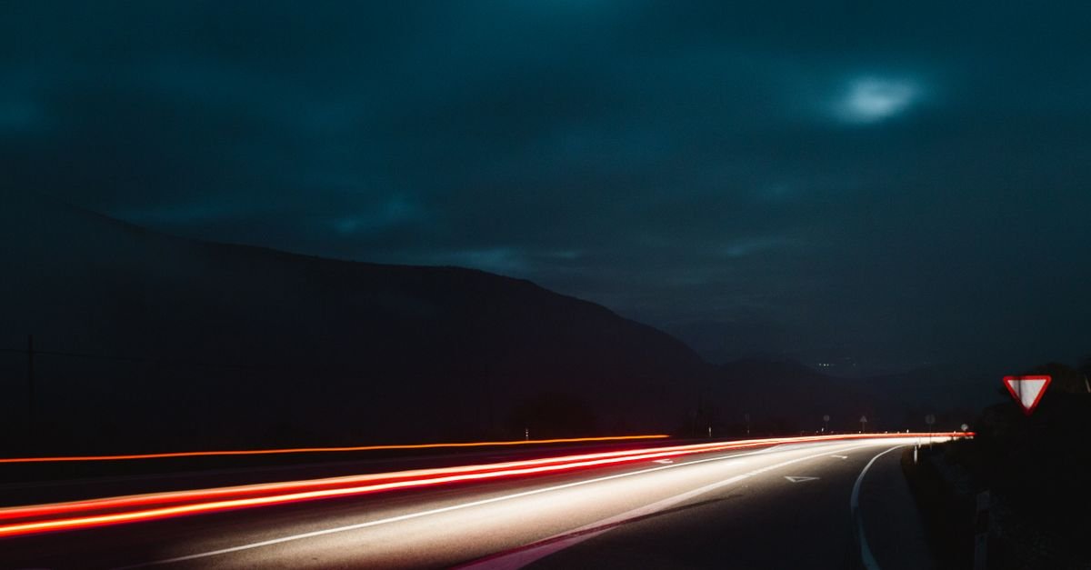 Rodovia à noite com rastros de luz vermelhos e brancos deixados por veículos em longa exposição