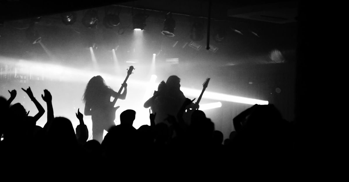 Silhueta de banda de rock tocando para plateia com braços erguidos sob luzes fortes