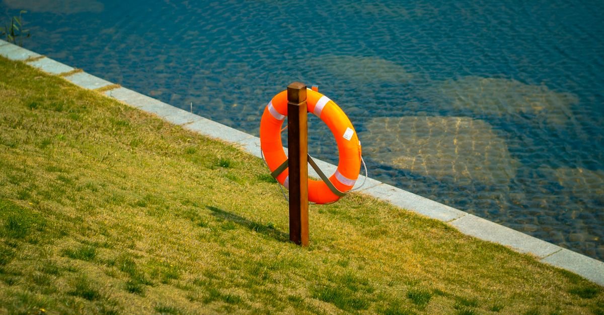 Boia salva-vidas laranja presa a um poste na margem gramada de um lago