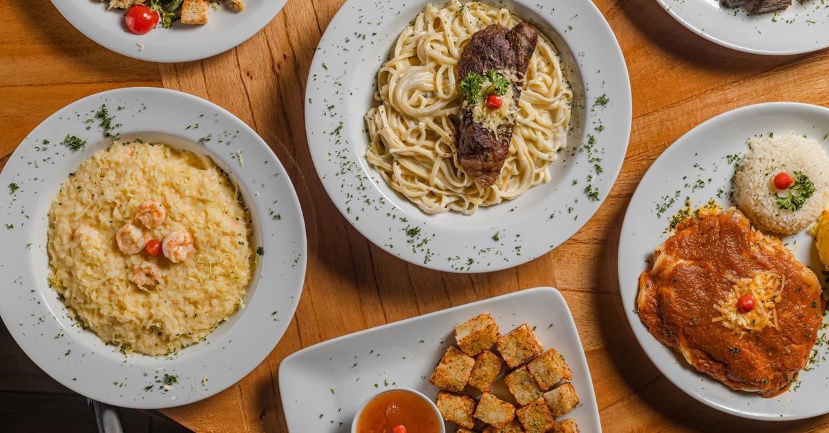 Mesa vista de cima com pratos de risoto de camarão, massa, parmegiana e petiscos
