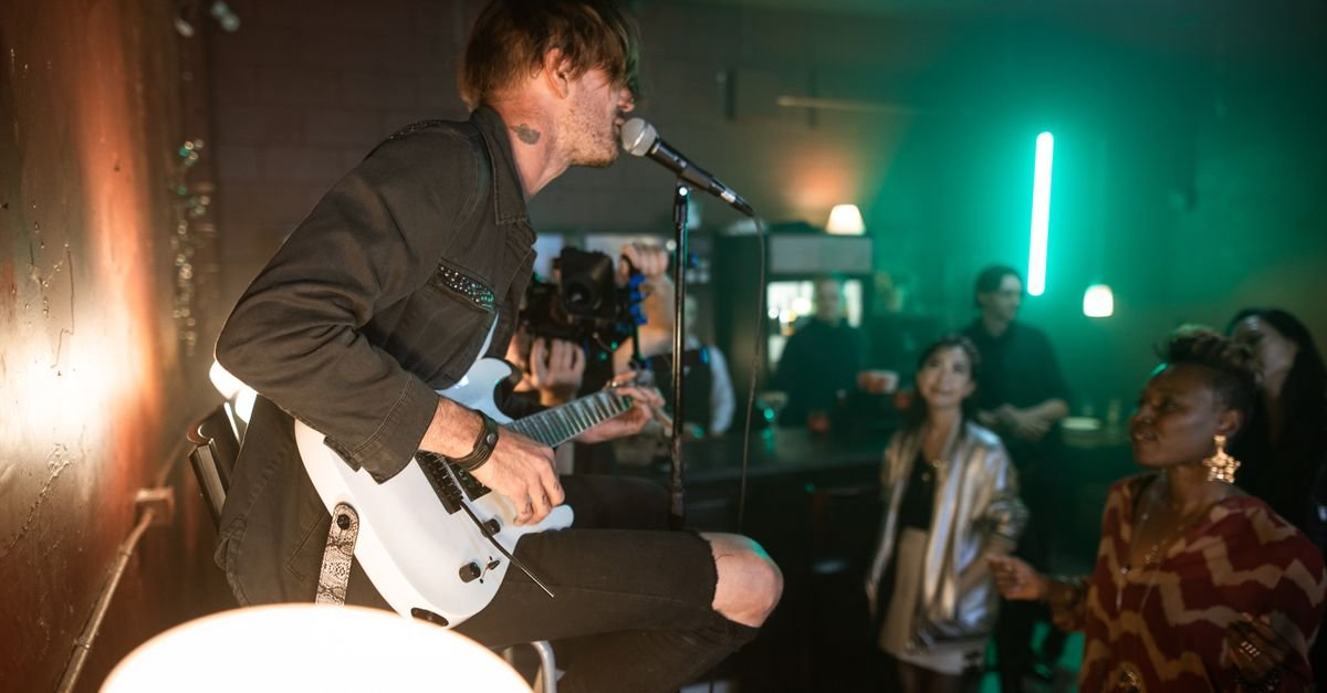 Guitarrista canta ao microfone durante show em bar, com público próximo ao palco