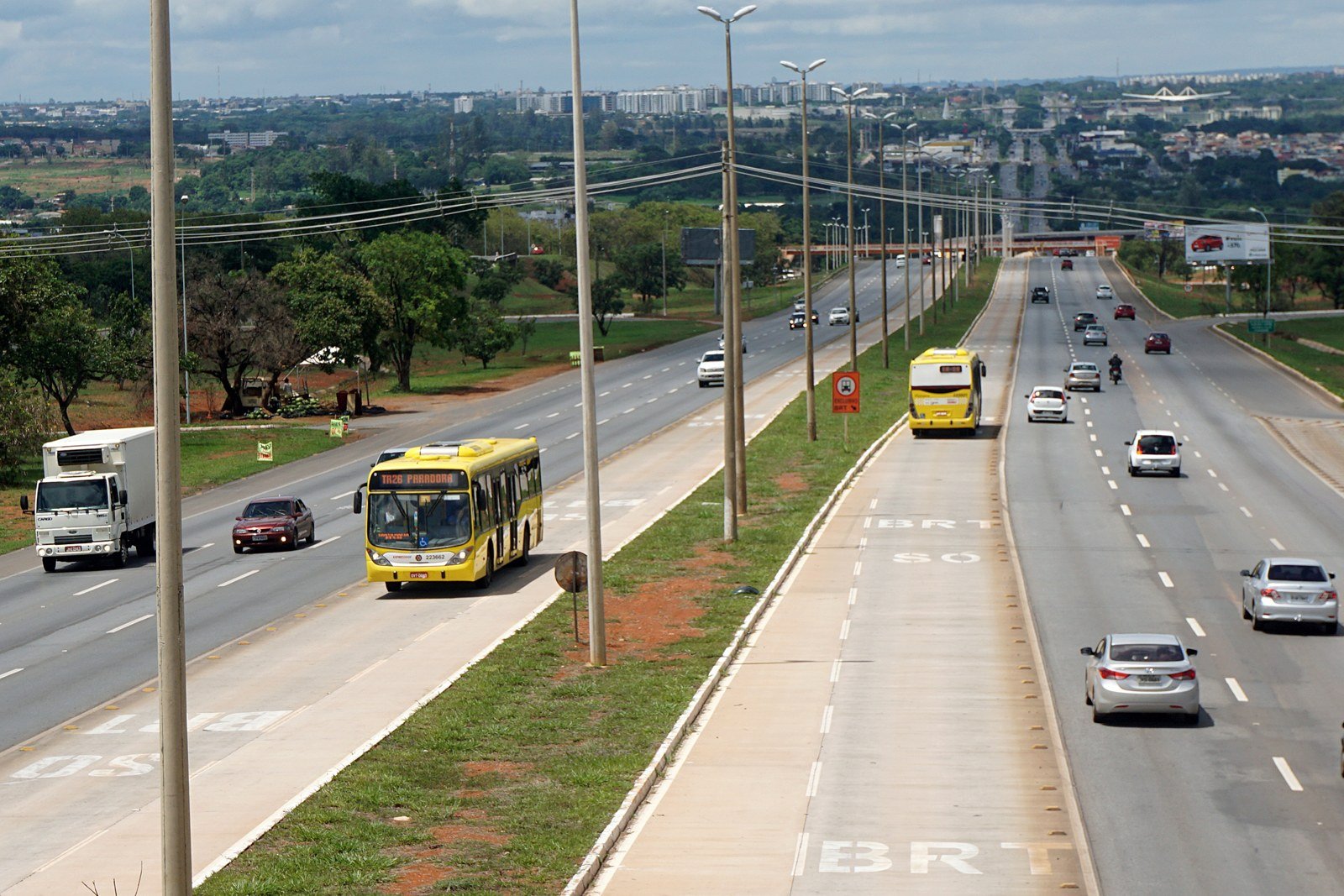Ônibus amarelo articulado no corredor exclusivo do BRT, com a pista pintada com a sigla BRT, em foto de 2016
