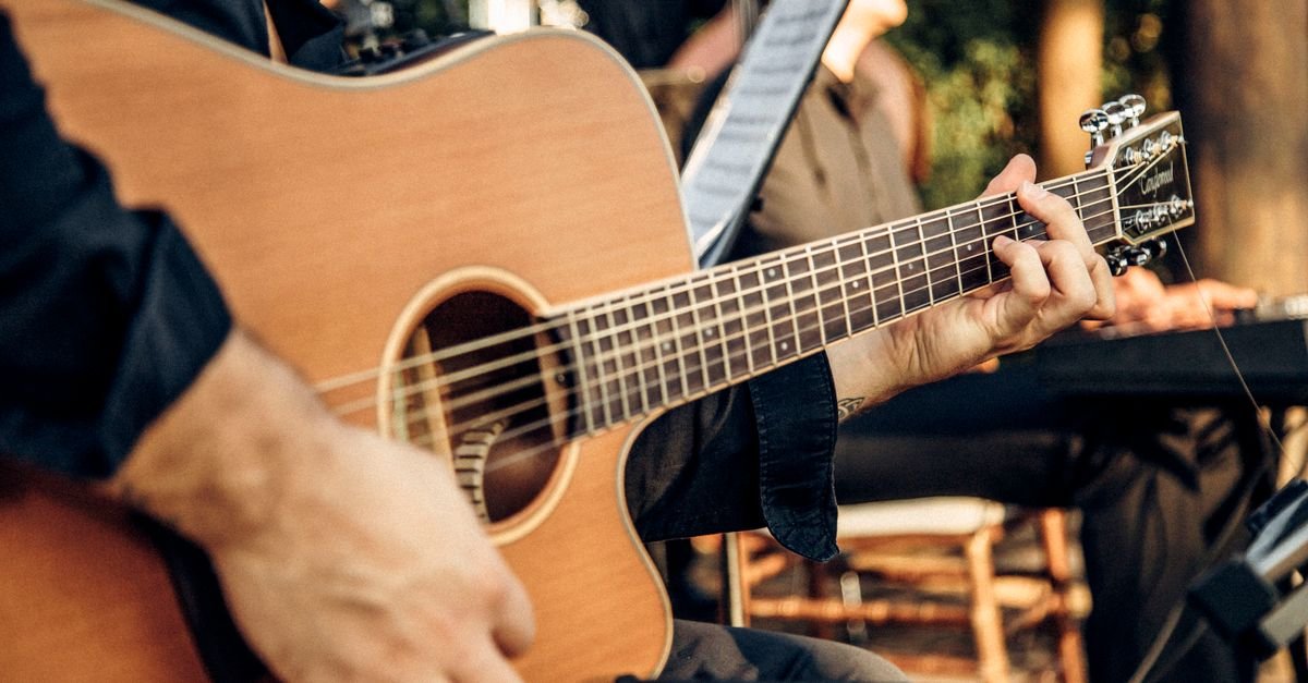 Mãos de um músico tocando violão de aço em apresentação ao vivo, em close