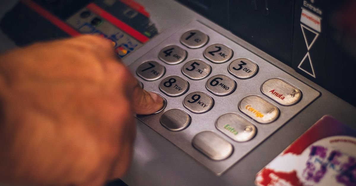 Mão digita a senha no teclado de um caixa eletrônico com teclas em português