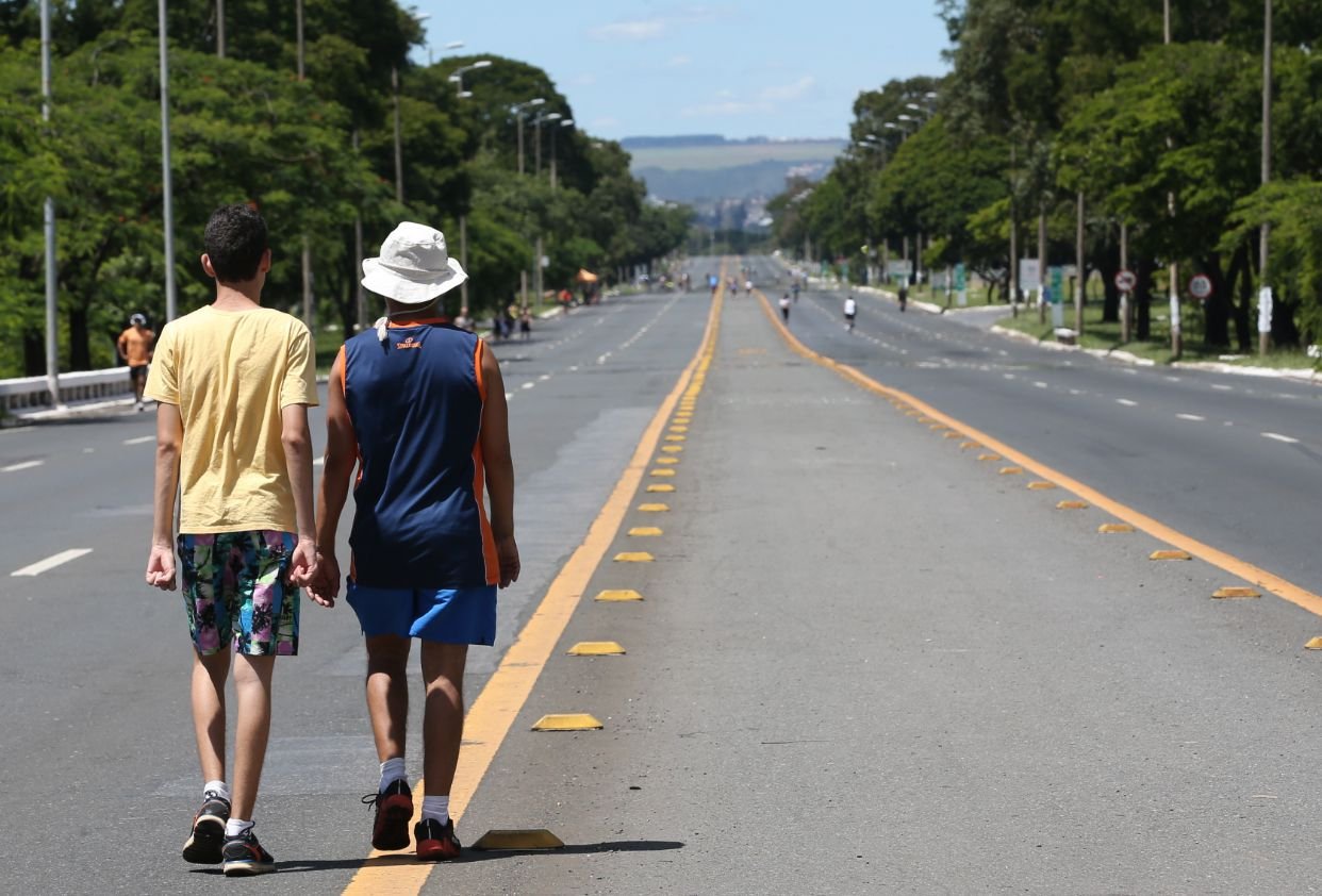 Pessoas caminhando pelo asfalto do Eixão do Lazer, em Brasília, em dia de sol