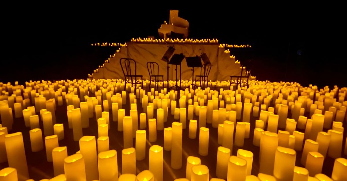 Palco iluminado por centenas de velas, com piano de cauda e estantes de partitura ao fundo