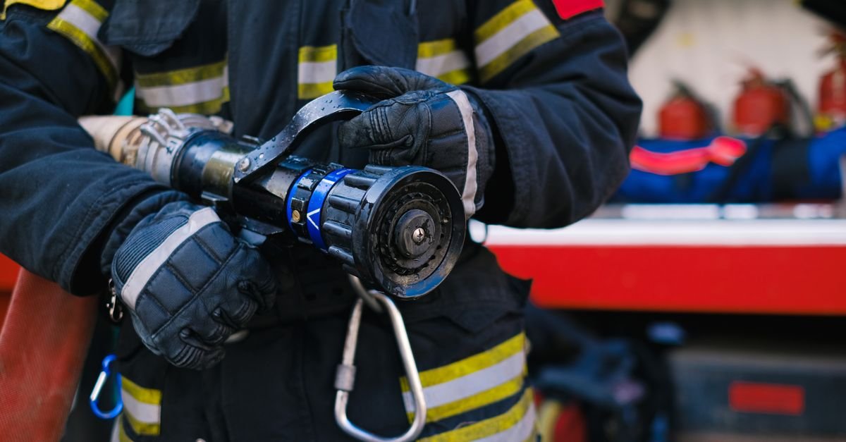 Close das maos enluvadas de um bombeiro segurando o esguicho de uma mangueira de combate a incendio