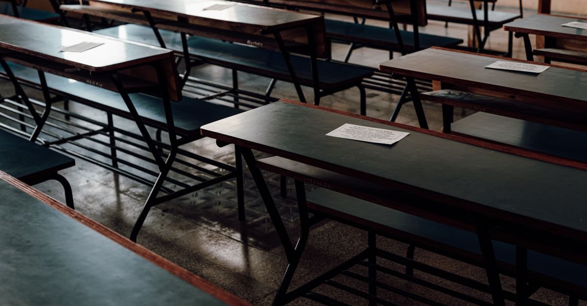 Fileiras de carteiras escolares vazias em sala de aula com piso de granilite