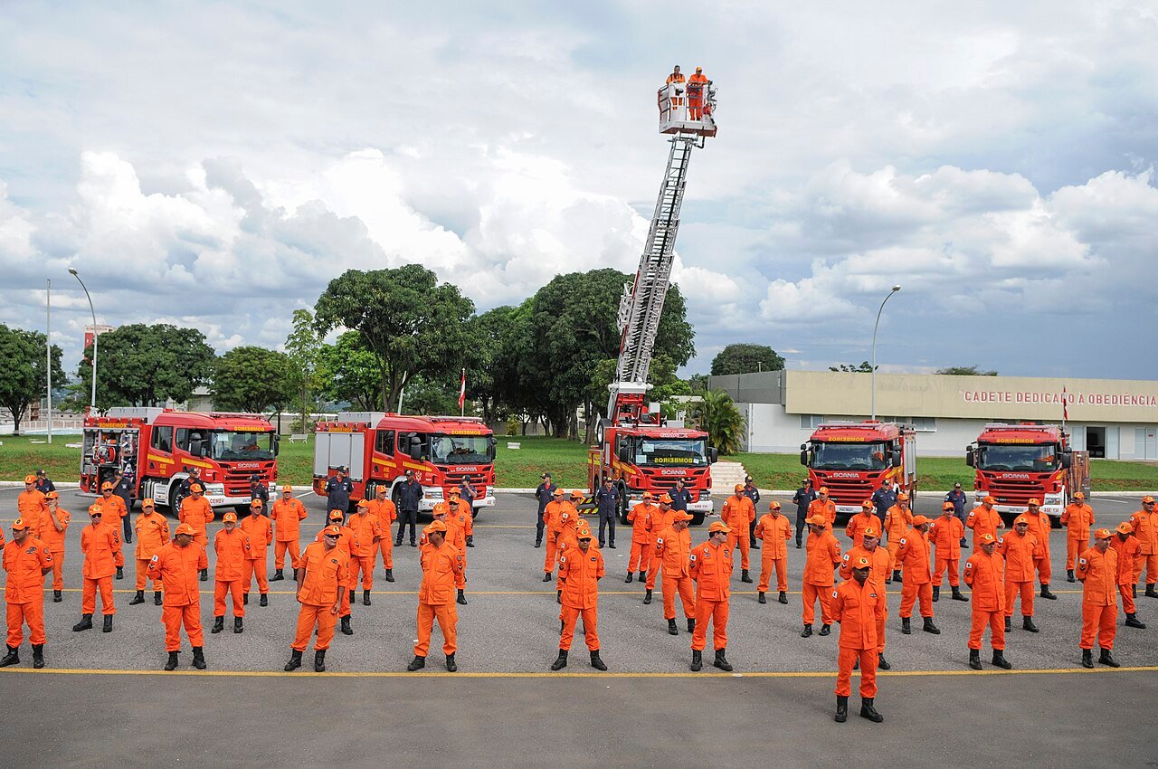 Militares do Corpo de Bombeiros do Distrito Federal em formatura diante de viaturas vermelhas e de uma escada Magirus estendida