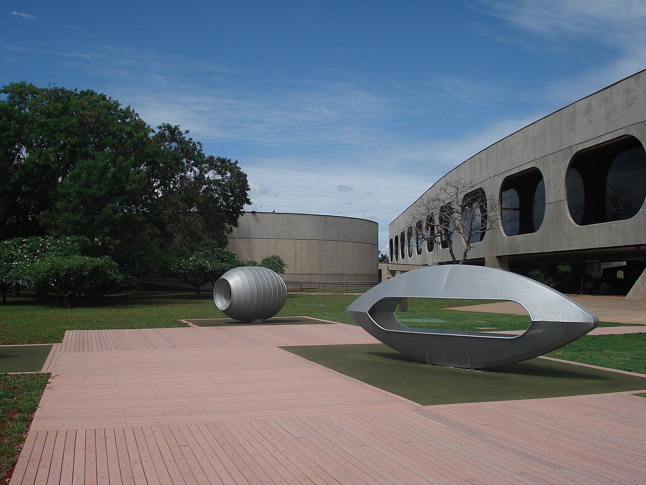 Área externa do Centro Cultural Banco do Brasil em Brasília, com esculturas metálicas sobre deck e a fachada circular de concreto ao fundo