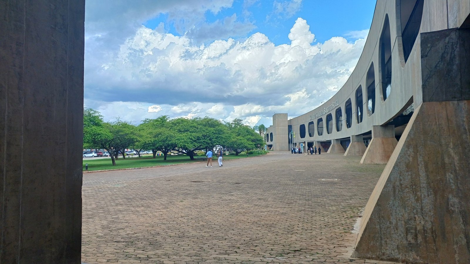 Fachada curva de concreto com janelas ovais do CCBB Brasília e a praça de pedra à frente