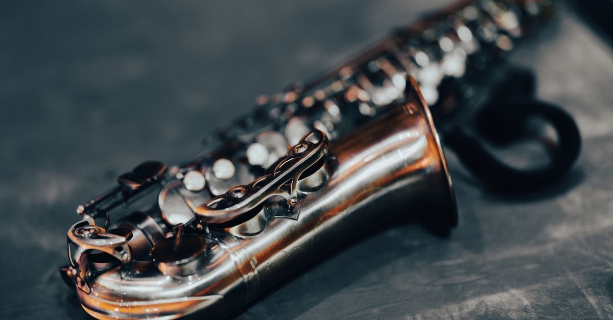 Close de um saxofone de corpo dourado apoiado sobre superficie escura