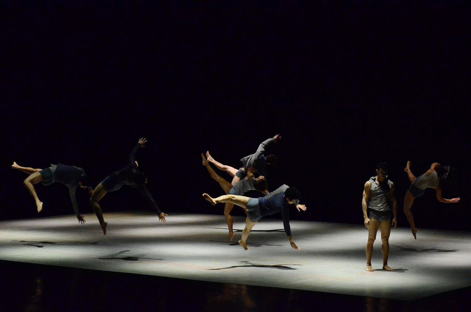 Bailarinos da Quasar Cia de Dança em salto sobre o palco iluminado por um facho de luz