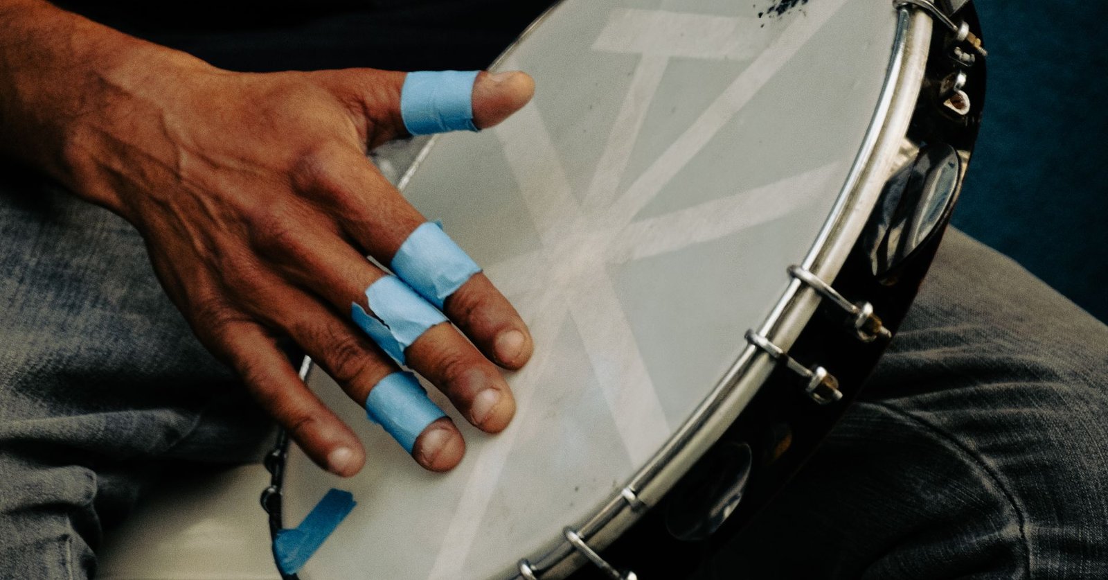 Mão com dedos protegidos por fita azul tocando um pandeiro; foto ilustrativa de pagode