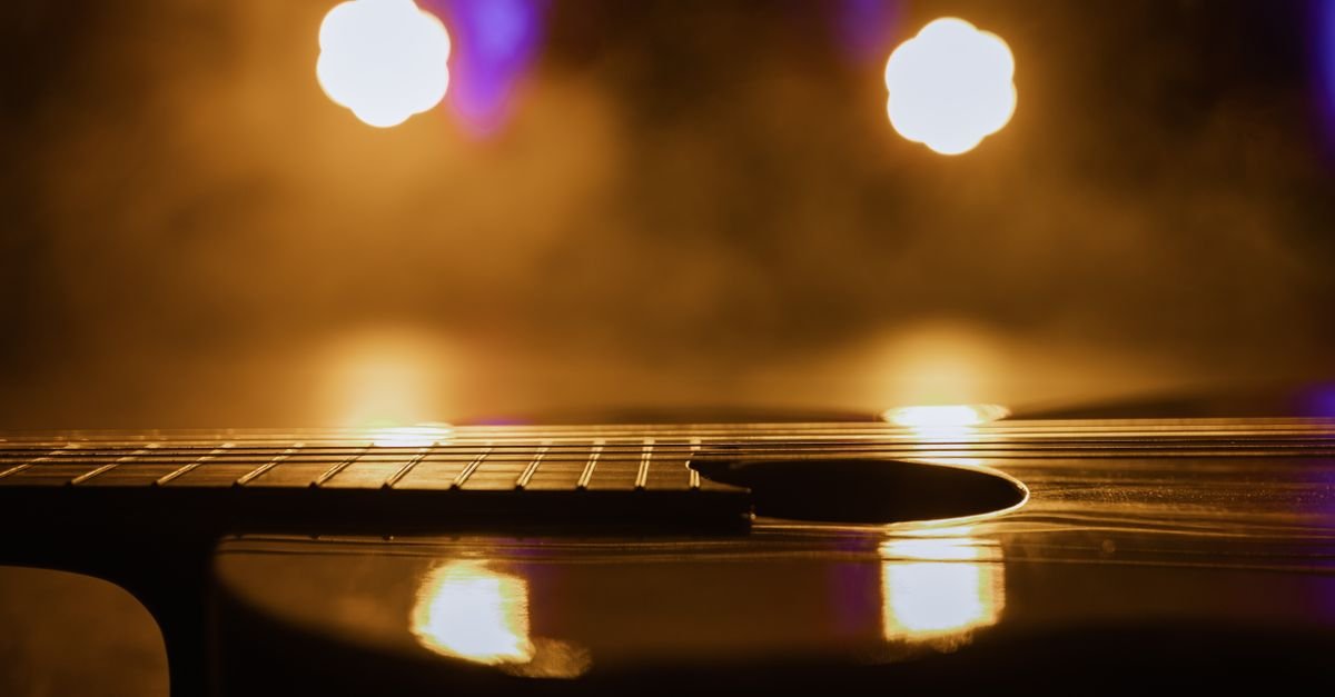 Violão em primeiro plano com luzes de palco desfocadas ao fundo